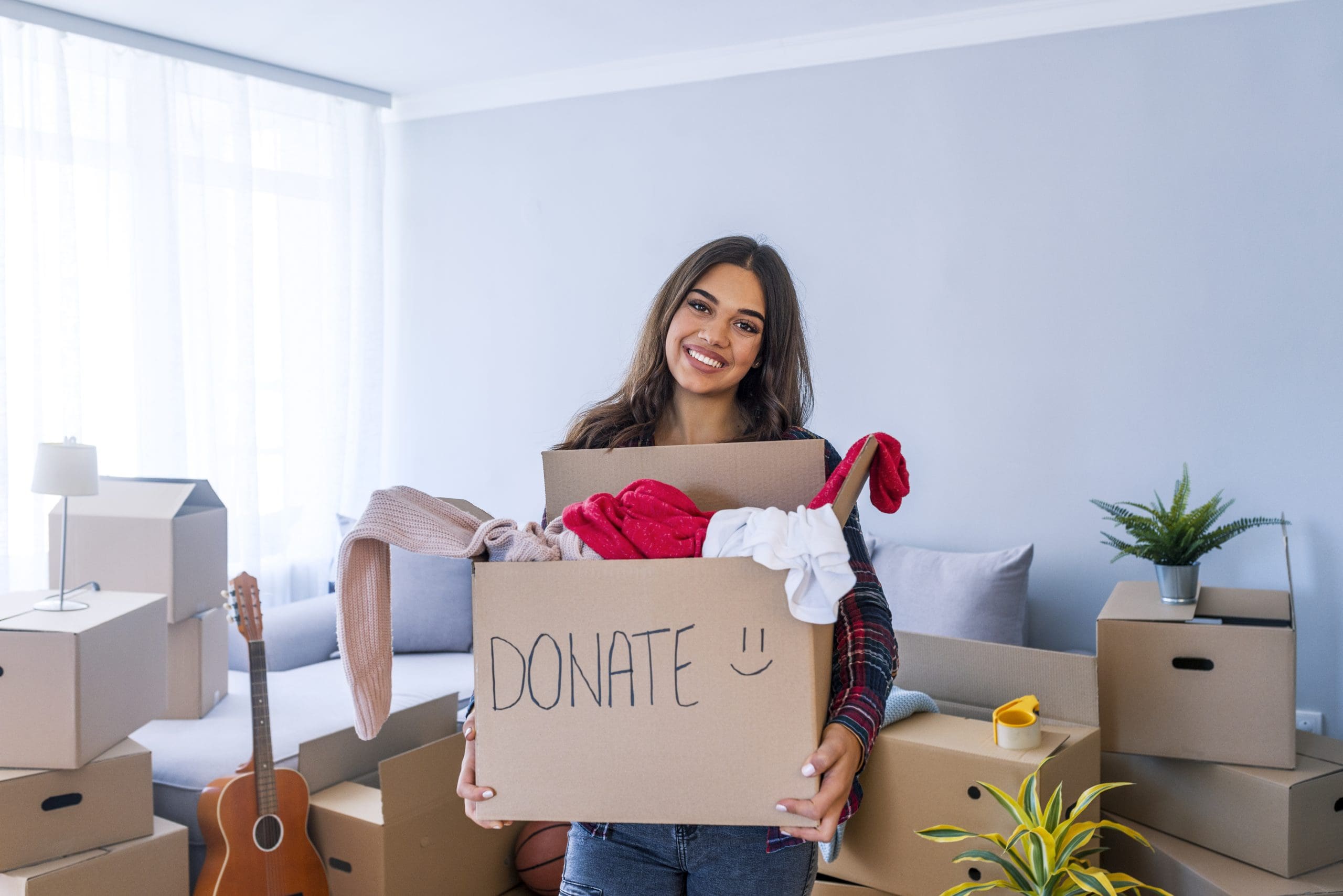 Donation Concept. Woman holding a Donate Box with full of Clothes. Woman holding a book and clothes donate box. Clothes in box for concept donation and reuse recycle